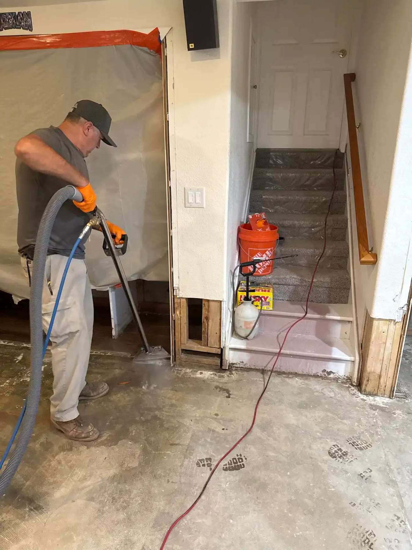 Technician extracting water at the foot of a basement stair next to a containment